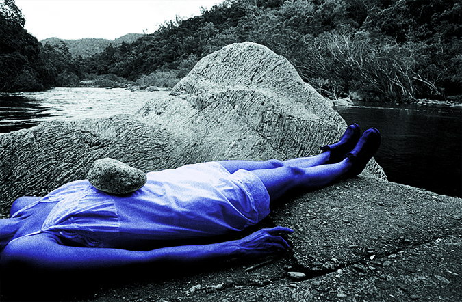 photograph of Rebecca Youdell lying in the foreground by on rocks by a river, by Glen O'Malley 1998