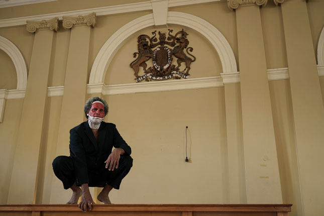 photograph of Zane Saunders sqatting on the Judges bench with the English coat of arms in the background.